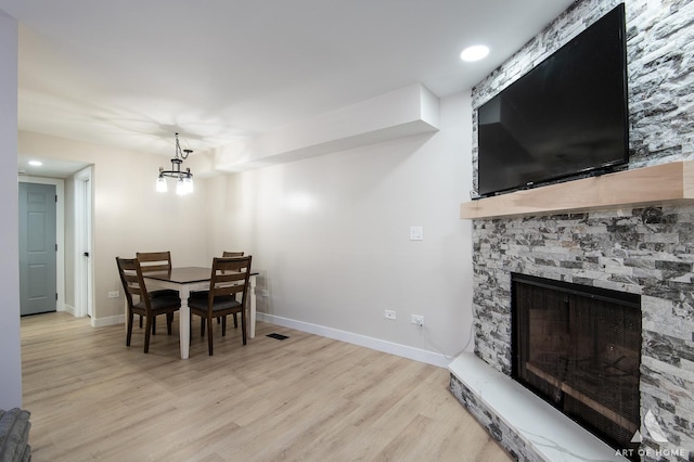 dining area featuring baseboards, a chandelier, a stone fireplace, recessed lighting, and light wood-style floors