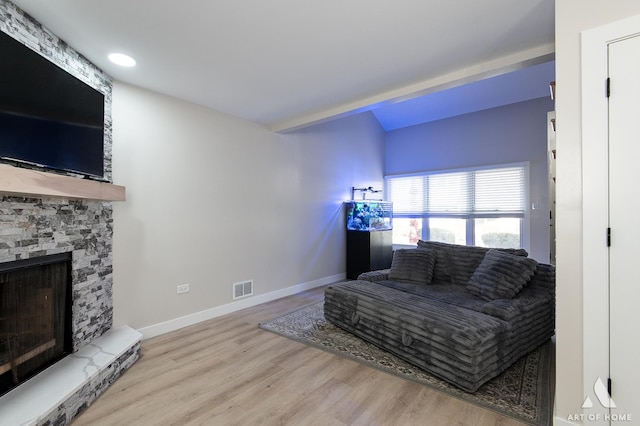 living room featuring a stone fireplace, wood finished floors, visible vents, and baseboards