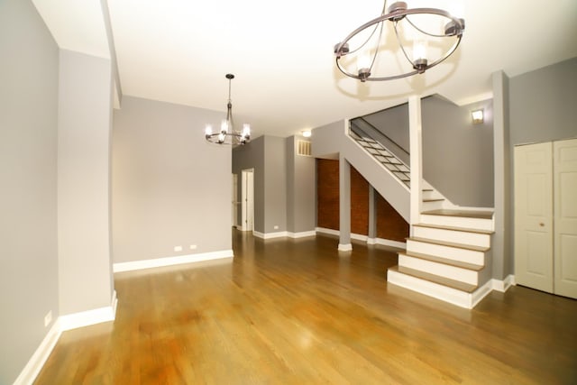 unfurnished living room featuring stairs, a notable chandelier, wood finished floors, and baseboards