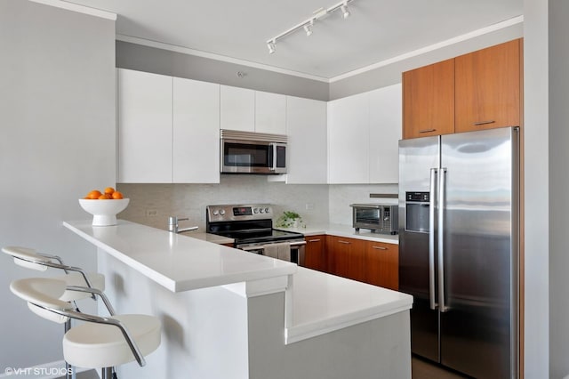 kitchen featuring tasteful backsplash, a breakfast bar, light countertops, appliances with stainless steel finishes, and a peninsula