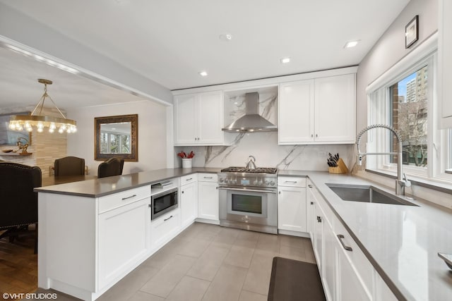 kitchen featuring a sink, tasteful backsplash, stainless steel appliances, a peninsula, and wall chimney range hood