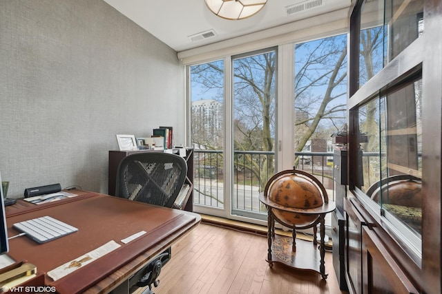 office space with visible vents, expansive windows, wallpapered walls, and wood finished floors