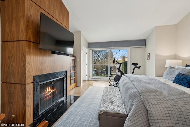 bedroom with access to outside, a lit fireplace, and wood finished floors