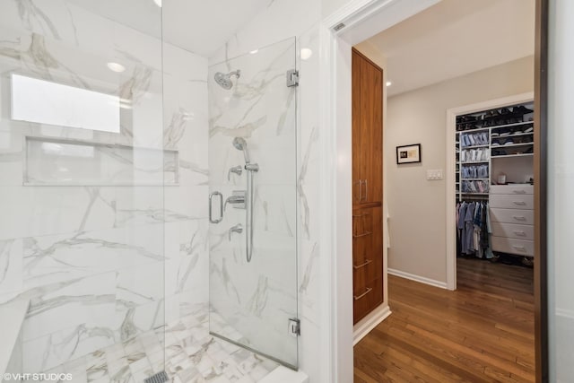 full bath with a marble finish shower, baseboards, wood finished floors, and a spacious closet