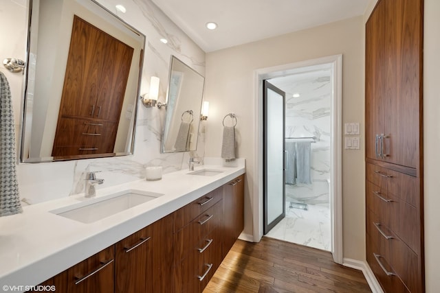 full bathroom featuring double vanity, backsplash, wood finished floors, and a sink