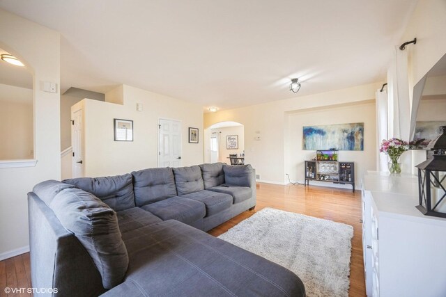 living room featuring light wood-style flooring, baseboards, and arched walkways