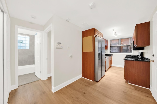 kitchen featuring dark countertops, brown cabinetry, stainless steel fridge with ice dispenser, and light wood-type flooring