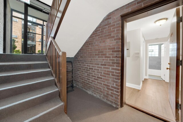 stairway featuring brick wall, baseboards, and wood finished floors