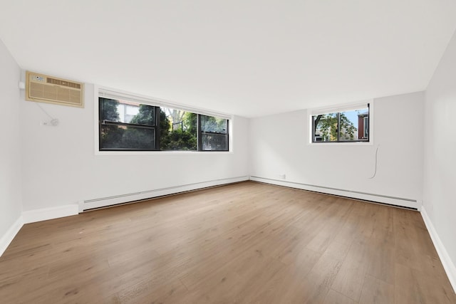 empty room featuring baseboard heating, a wall mounted AC, baseboards, and wood finished floors