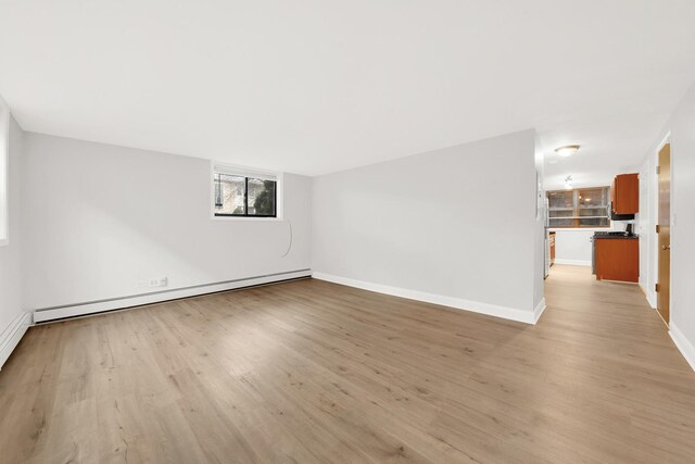 empty room featuring light wood-type flooring, baseboards, and baseboard heating