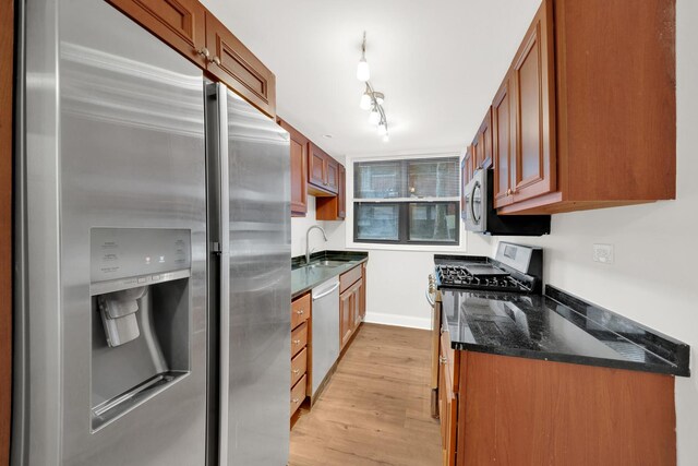 kitchen featuring dark stone countertops, baseboards, light wood finished floors, stainless steel appliances, and brown cabinets