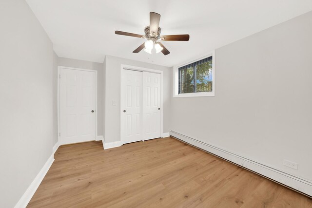 unfurnished bedroom featuring a baseboard heating unit, baseboards, light wood-style floors, a closet, and a ceiling fan