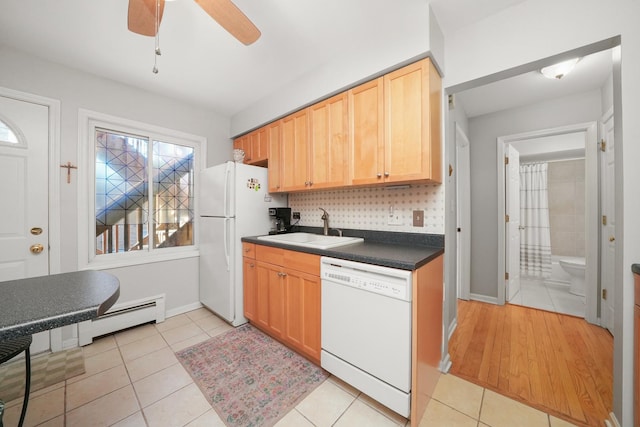 kitchen with dark countertops, light tile patterned floors, baseboard heating, white appliances, and a sink
