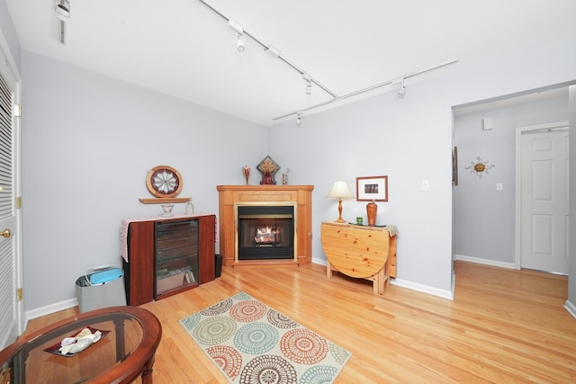living room featuring track lighting, a warm lit fireplace, baseboards, and wood finished floors