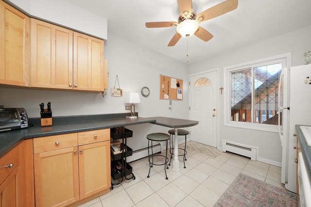 kitchen featuring dark countertops, light brown cabinets, baseboard heating, freestanding refrigerator, and light tile patterned flooring