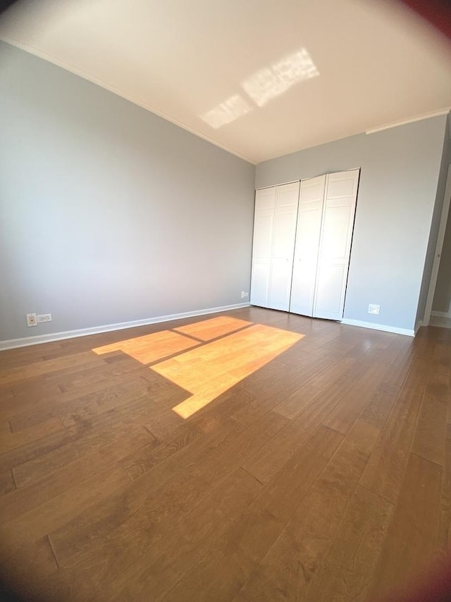 unfurnished bedroom featuring dark wood-type flooring, crown molding, and baseboards