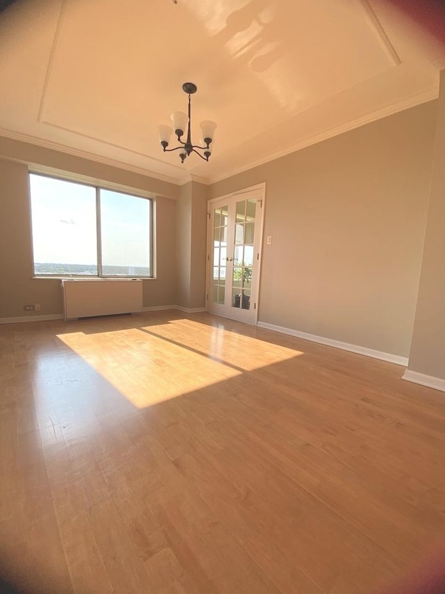 empty room with a chandelier, wood finished floors, baseboards, and ornamental molding