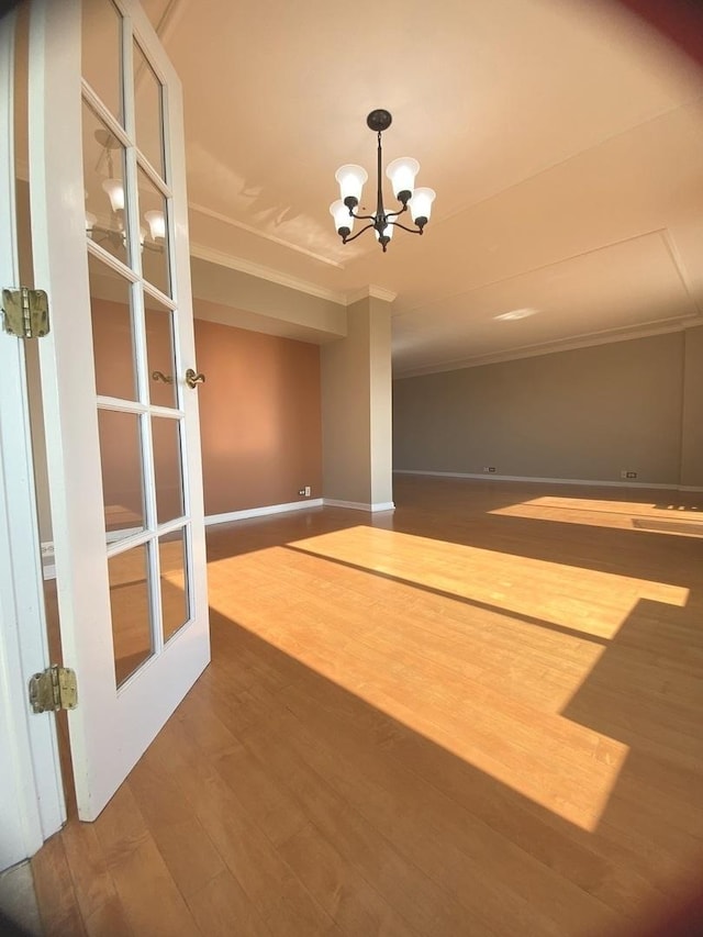 interior space featuring baseboards, a notable chandelier, wood finished floors, and ornamental molding