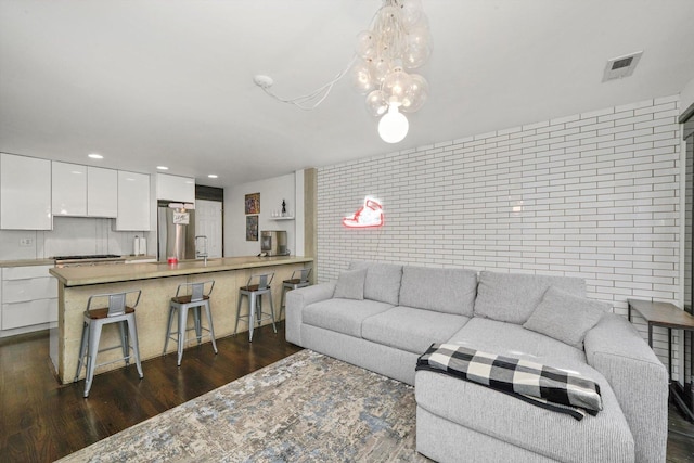 living area featuring dark wood finished floors, visible vents, recessed lighting, and brick wall