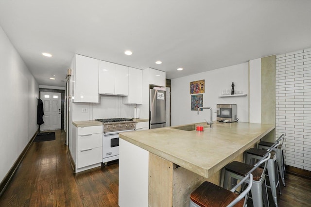 kitchen with a sink, freestanding refrigerator, range with gas cooktop, a peninsula, and a breakfast bar area