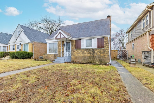 view of front of home featuring a shingled roof, a front yard, brick siding, and a chimney