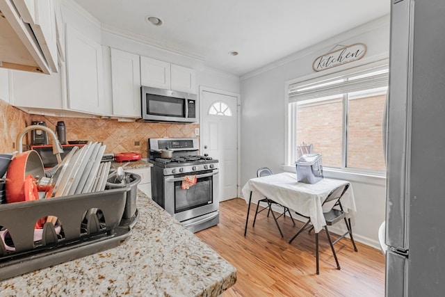 kitchen featuring decorative backsplash, light wood-style floors, appliances with stainless steel finishes, white cabinetry, and crown molding