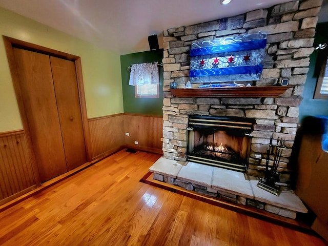 unfurnished living room featuring a wainscoted wall, a stone fireplace, and wood finished floors