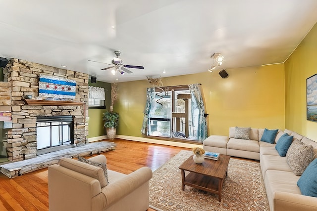 living area with baseboards, a stone fireplace, wood finished floors, and a ceiling fan