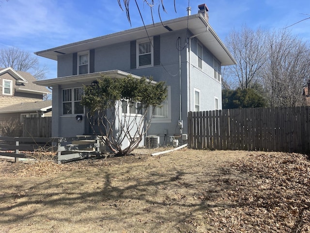 view of front facade with stucco siding, cooling unit, a chimney, and fence