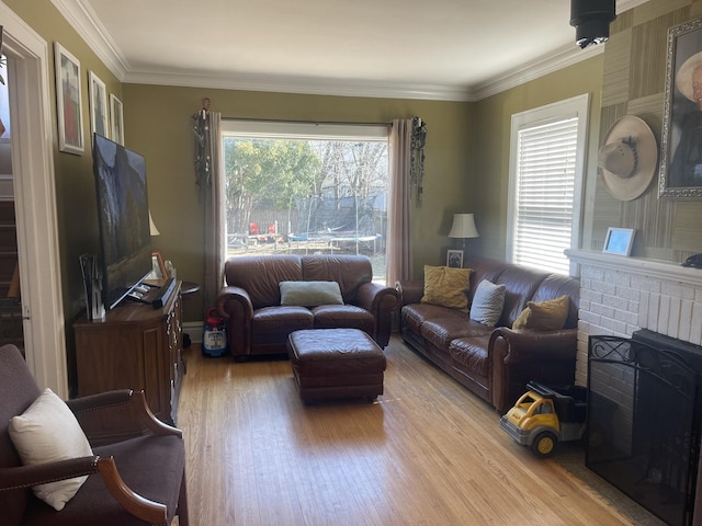 living area with a fireplace, crown molding, wood finished floors, and a healthy amount of sunlight