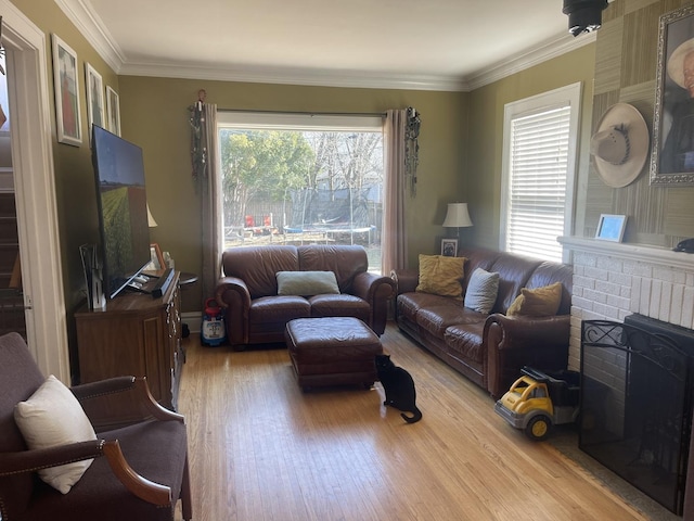 living area featuring a healthy amount of sunlight, a fireplace, ornamental molding, and wood finished floors