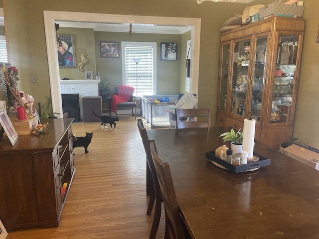 dining area featuring a brick fireplace, light wood-style flooring, and crown molding