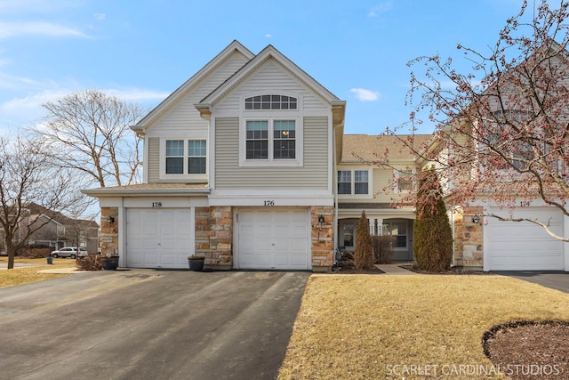 traditional-style house featuring a garage, stone siding, a front yard, and driveway