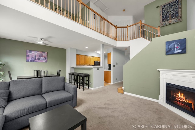 living area with a ceiling fan, baseboards, a high ceiling, light carpet, and a glass covered fireplace