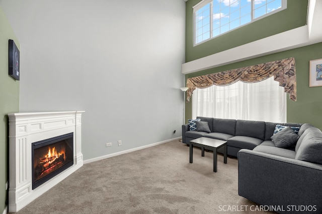 living area featuring baseboards, carpet floors, a high ceiling, and a warm lit fireplace