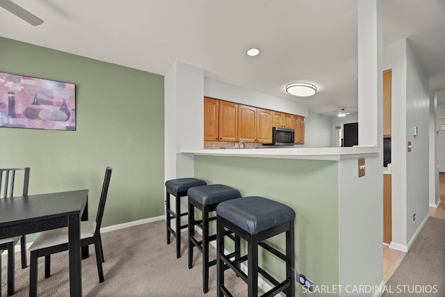 kitchen featuring brown cabinetry, baseboards, light carpet, a kitchen bar, and stainless steel microwave