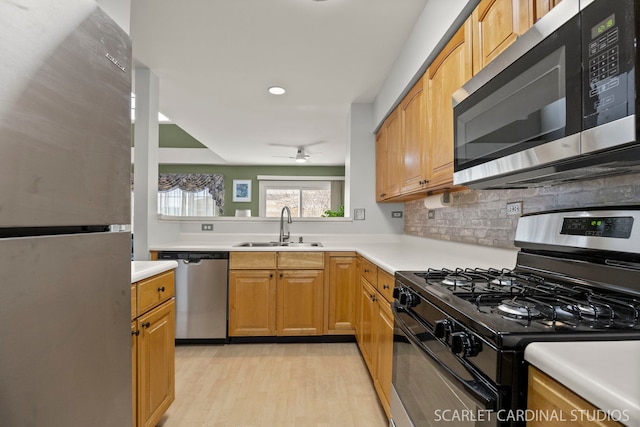 kitchen featuring light wood-type flooring, a sink, light countertops, appliances with stainless steel finishes, and tasteful backsplash