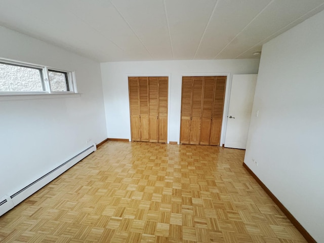 unfurnished bedroom featuring a baseboard heating unit, multiple closets, and baseboards