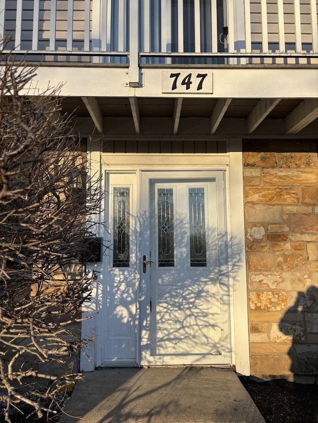 property entrance featuring stone siding and a balcony