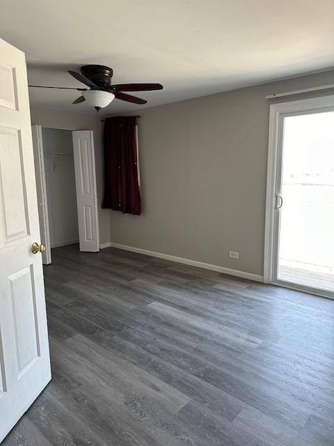 unfurnished room with dark wood finished floors, a ceiling fan, and baseboards