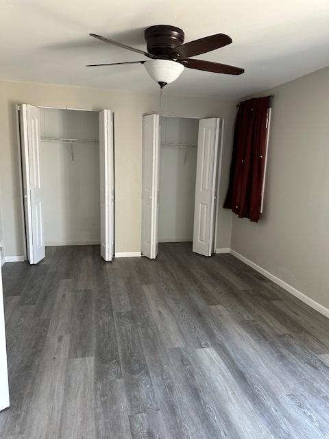 unfurnished bedroom featuring ceiling fan, dark wood-style floors, multiple closets, and baseboards