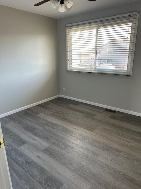 unfurnished room featuring visible vents, a ceiling fan, dark wood-type flooring, and baseboards