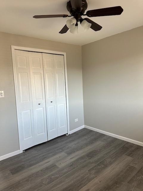 unfurnished bedroom with dark wood finished floors, a ceiling fan, baseboards, and a closet