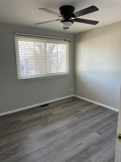 empty room with visible vents, baseboards, dark wood-style floors, and a ceiling fan