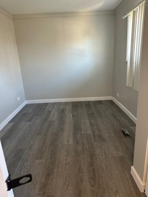 empty room with dark wood finished floors, visible vents, baseboards, and ornamental molding