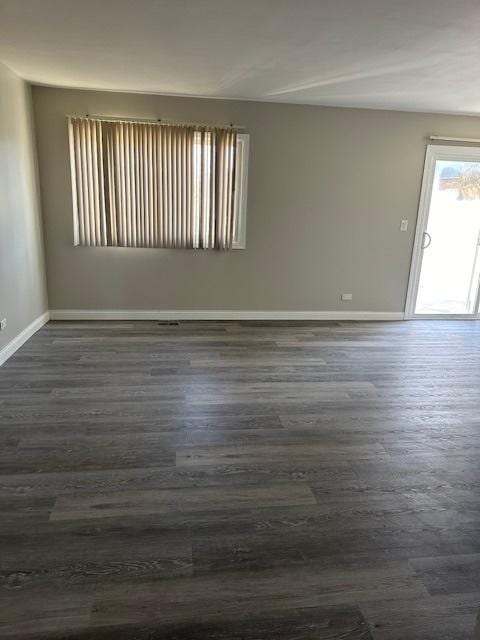 spare room with baseboards and dark wood-type flooring