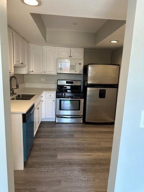 kitchen featuring a sink, white cabinetry, stainless steel appliances, light countertops, and dark wood-style flooring