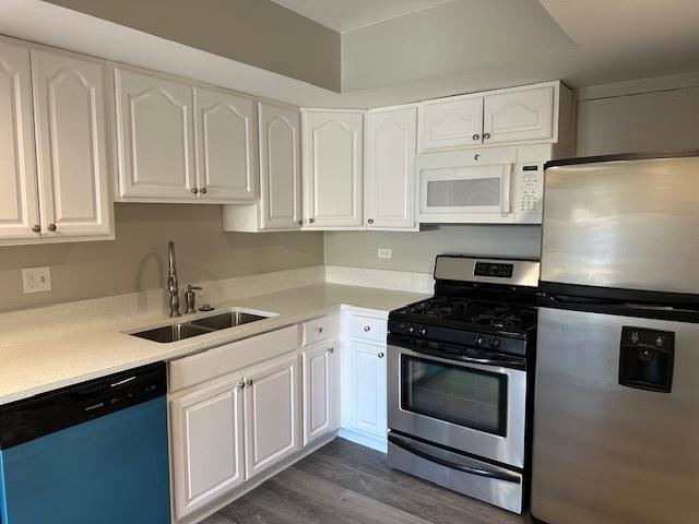 kitchen with a sink, stainless steel appliances, light countertops, dark wood-type flooring, and white cabinetry