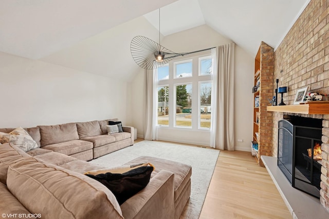 living area featuring baseboards, an inviting chandelier, lofted ceiling, light wood-style flooring, and a brick fireplace