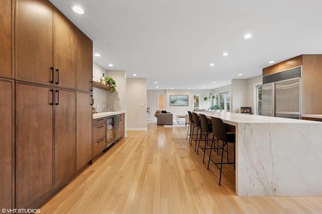 kitchen featuring light wood finished floors, a kitchen breakfast bar, built in refrigerator, and open shelves